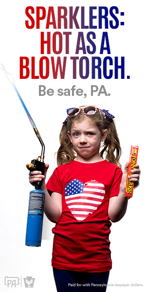 A little girl wearing pigtails holds a blowtorch in one hand and a box of sparklers in the other..